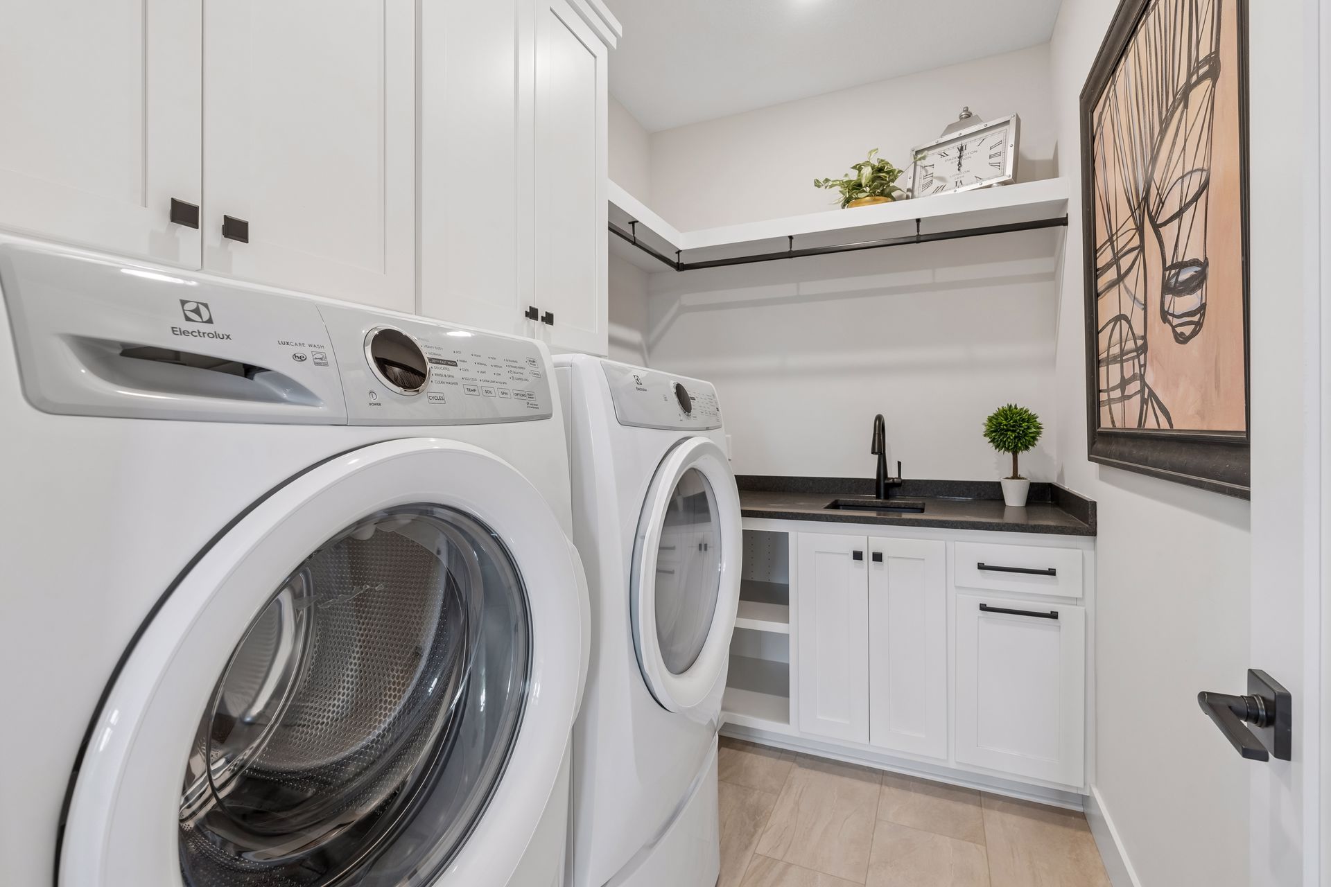Main floor laundry room with utility sink, storage cabinets and front load appliances